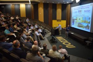 A presenter speaks to an audience in an auditorium