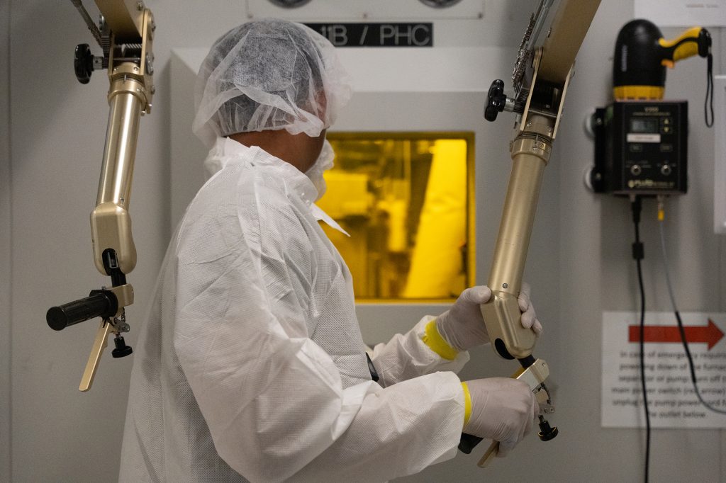 A nuclear manufacturing technician works with a remote manipulator arm in a hot cell