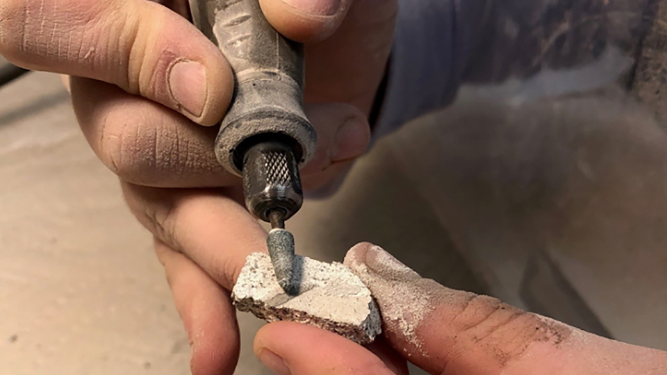 A pottery sample is being burred with a handheld tool.